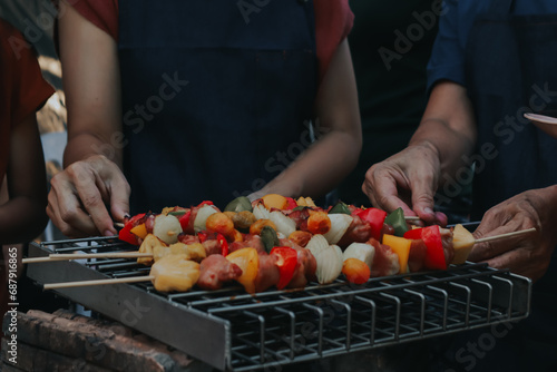 People are cooking seafood and vegetable skewers on a charcoal grill. with a plate of shrimp placed next to it A warm family holiday celebration. BBQ party