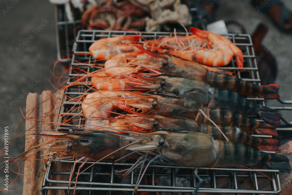 People are cooking seafood and vegetable skewers on a charcoal grill. with a plate of shrimp placed next to it A warm family holiday celebration. BBQ party