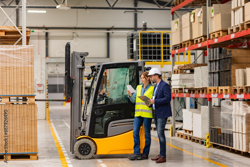 Female forklift driver, warehouse worker talking with manager, standing by forklift. Warehouse worker preparing products for shipmennt, delivery, checking stock in warehouse.