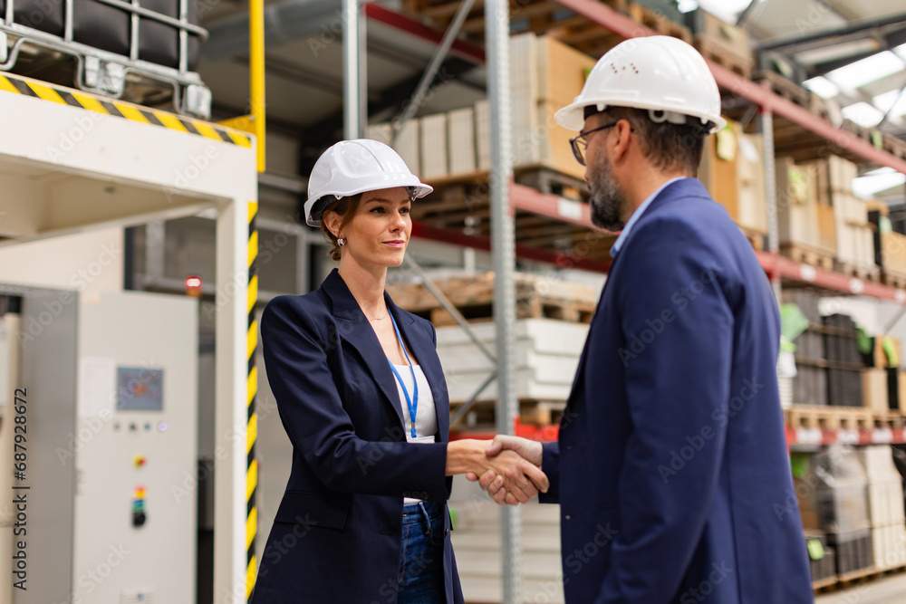 Female engineer and male project manager shaking hands in modern industrial factory. Manufacturing facility with robotics and automation. Women in manufacturing. Female engineer and male project manager shaking hands in modern industrial factory. Manufacturing facility with robotics and automation. Women in manufacturing.