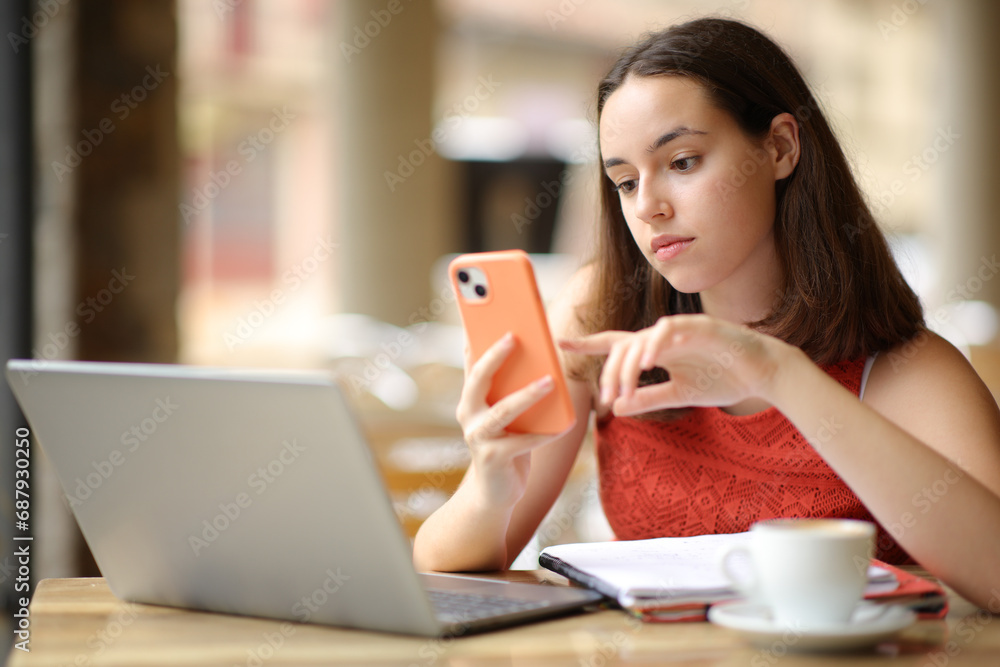 Serious woman checking phone and laptop in a bar Serious woman checking phone and laptop in a bar