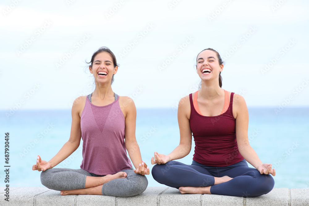 Two yogis laughing doing yoga on the beach