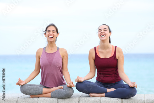 Two yogis laughing doing yoga on the beach