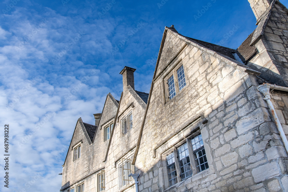 Low angle view of façade of traditional and typical building of Painswick, UK, known as the Queen of the Cotswolds, mainly built from the honey colored Cotswold Stone against a white clouded blue sky