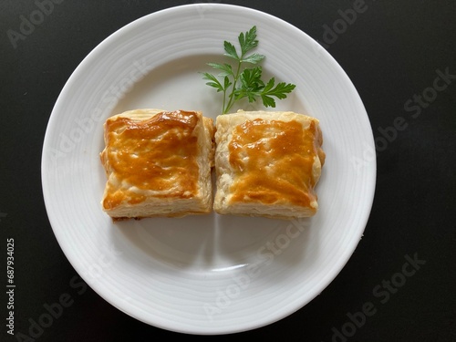 2 quadratische gefüllte Blätterteigtaschen mit Petersilie garniert auf einem weissen Teller angerichtet, kleiner Snack für Zwischendurch