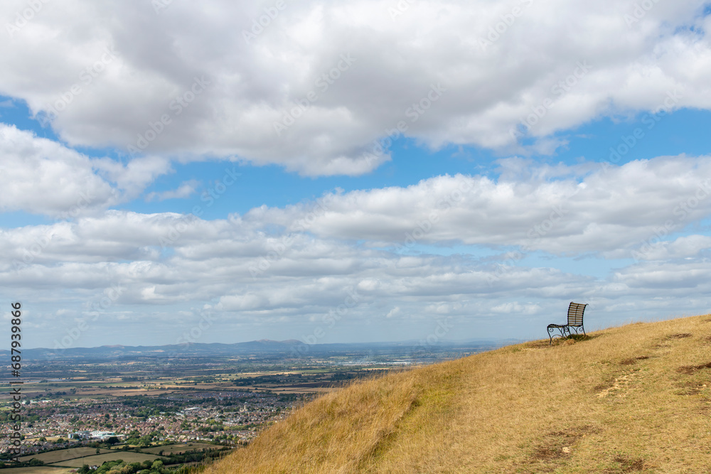 View of a single empty bench on top of Cleeve Hill, Cheltenham, UK along the public footpath Cotswold way with panoramic view on the valley and outskirts of city of Cheltenham