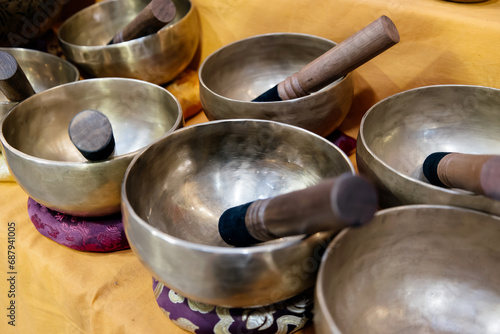 Traditional Tibetan singing bowls on a vibrant yellow fabric, each with a wooden mallet resting inside or beside it. Sound healing therapies, meditation sessions, and spiritual rituals. 