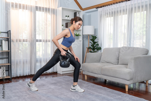 Vigorous energetic woman doing kettlebell weight lifting exercise at home. Young athletic asian woman strength and endurance training session as home workout routine.