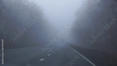 A bus with its headlights on is driving in the fog along on an asphalt road