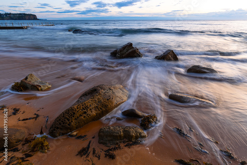 Fototapeta Naklejka Na Ścianę i Meble -  Water flowing between rocks on the sandy shore with cloudy sky.