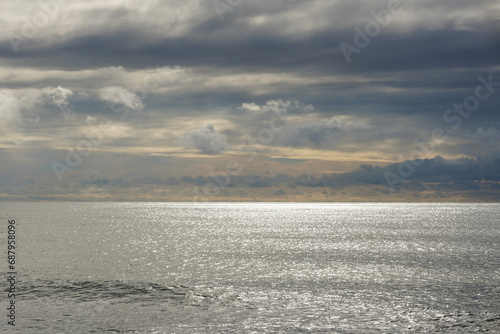 Soft view of the sun behind the rainy clouds over the calm sea. 