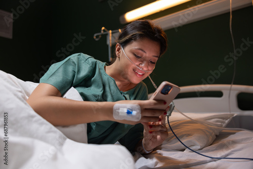 Sick girl in an oxygen tube holds a phone in her hands  laughs  looks at photos in social networks  has fun while being treated.