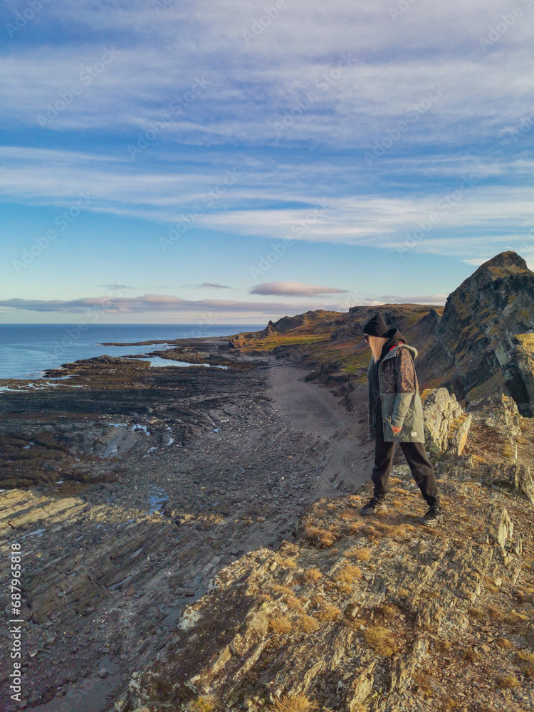 A woman on the background of the rocky coast of the Barents Sea. Beautiful view of the cliffs and the coast of the Rybachy and Sredny peninsulas. The harsh beauty of the north.