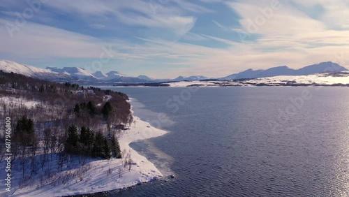 Snow covered mountain range on coastline in winter, Norway. Surroundings of town Tromso. Panoramic aerial view landscape of nordic snow cowered mountains, houses and ocean. Troms county, Fjordgard photo