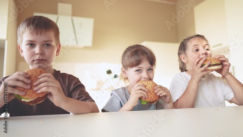 children eat burgers. fast food burger. a group of small children in the kitchen greedily eat fast food burgers. big family small kids having breakfast in the morning in the kitchen eating fun burger