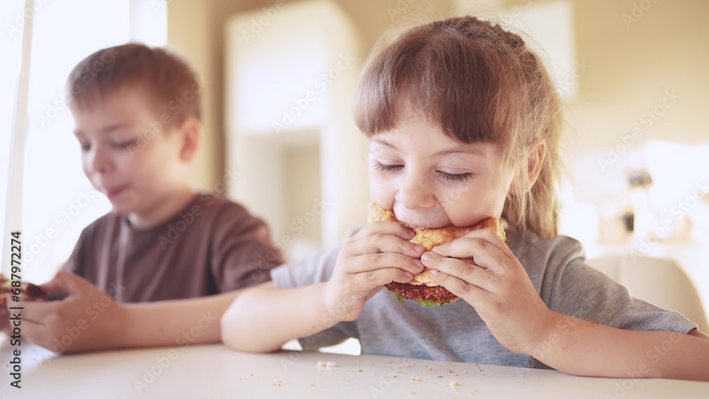 children eat burgers. fast food burger. a group of small children in the kitchen greedily eat fast food burgers. big family small kids having breakfast in the morning in sun the kitchen eating burger children eat burgers. fast food burger. a group of small children in the kitchen greedily eat fast food burgers. big family small kids having breakfast in the morning in sun the kitchen eating burger