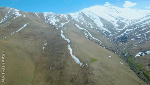 Aerial view of high mountains covered with snow with thawing on a sunny day against a sky. Deserted gray mountains in winter without grass with snowy peaks. Drone footage. Movement in an arc. Armenia