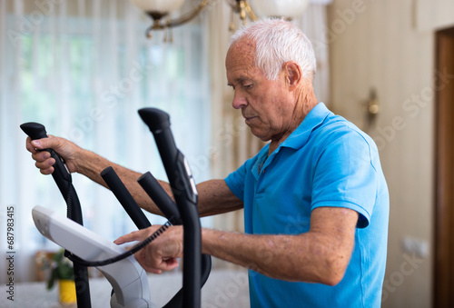 Positive senior man works out on an elliptical machine at home