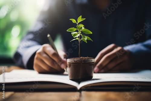 Businessman holding a pencil and plant in a pot on the book, eco and save the earth concept