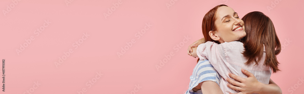 cheerful woman with closed eyes embracing teenage girl on pink backdrop, horizontal banner cheerful woman with closed eyes embracing teenage girl on pink backdrop, horizontal banner