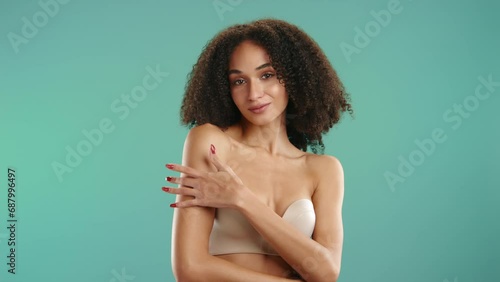 Cute curly-haired sexual lady in strapless bra with mouth slightly open seductively running her fingers on shoulder and neck isolated on green background. High quality 4k footage photo