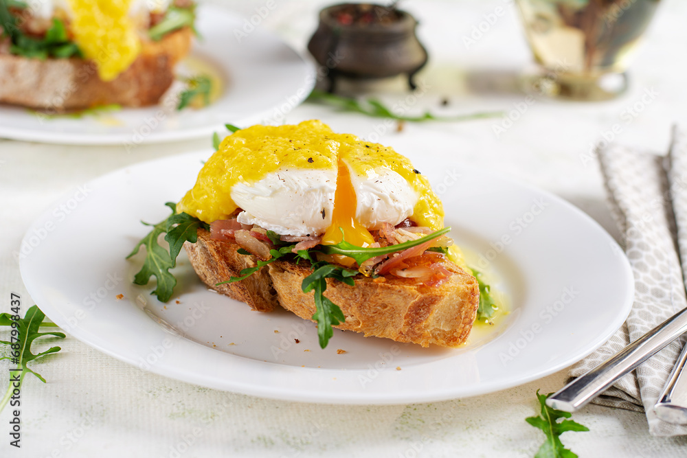 Breakfast. Sandwich with ham, poached egg, onion and arugula in a plate on a light background