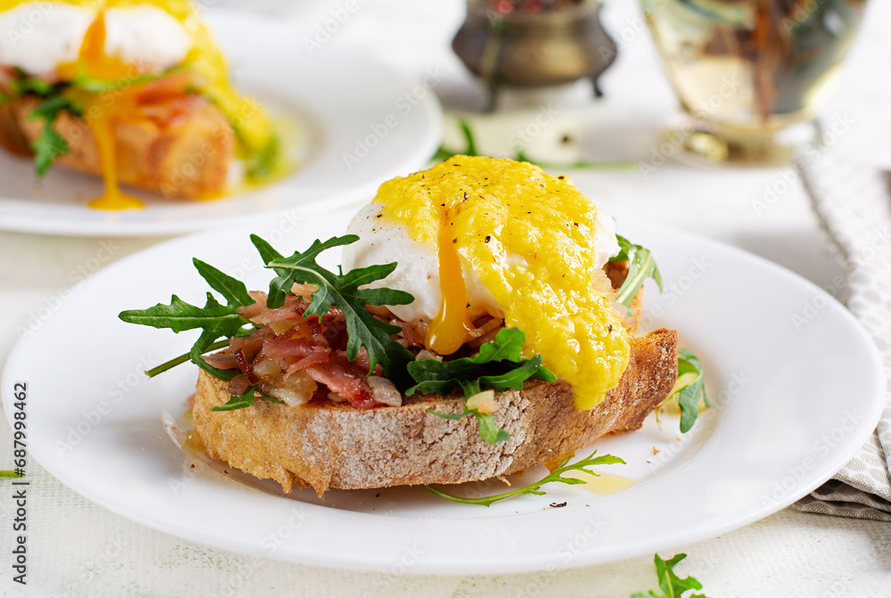 Breakfast. Sandwich with ham, poached egg, onion and arugula in a plate on a light background Breakfast. Sandwich with ham, poached egg, onion and arugula in a plate on a light background