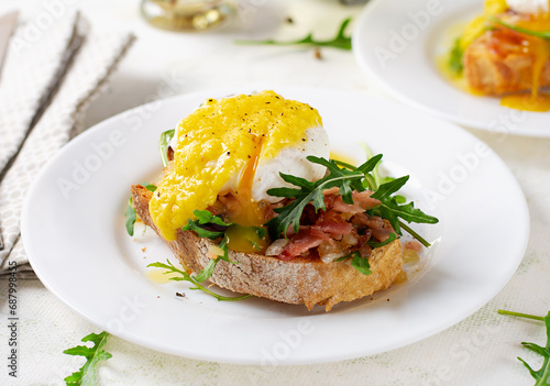 Breakfast. Sandwich with ham, poached egg, onion and arugula in a plate on a light background