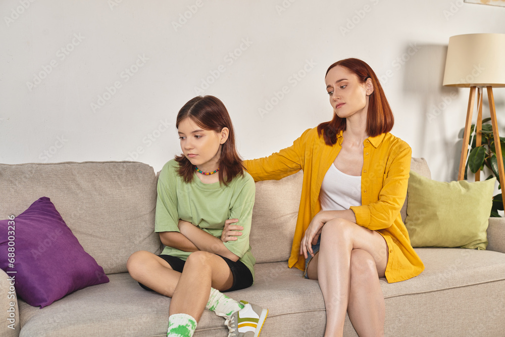upset teenage girl sitting near thoughtful mother on couch in living room, supportive parent upset teenage girl sitting near thoughtful mother on couch in living room, supportive parent