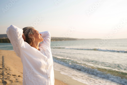 Mature woman with hands behind head standing at beach photo