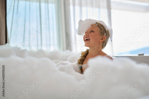 Smiling girl playing with soap suds in bathtub photo