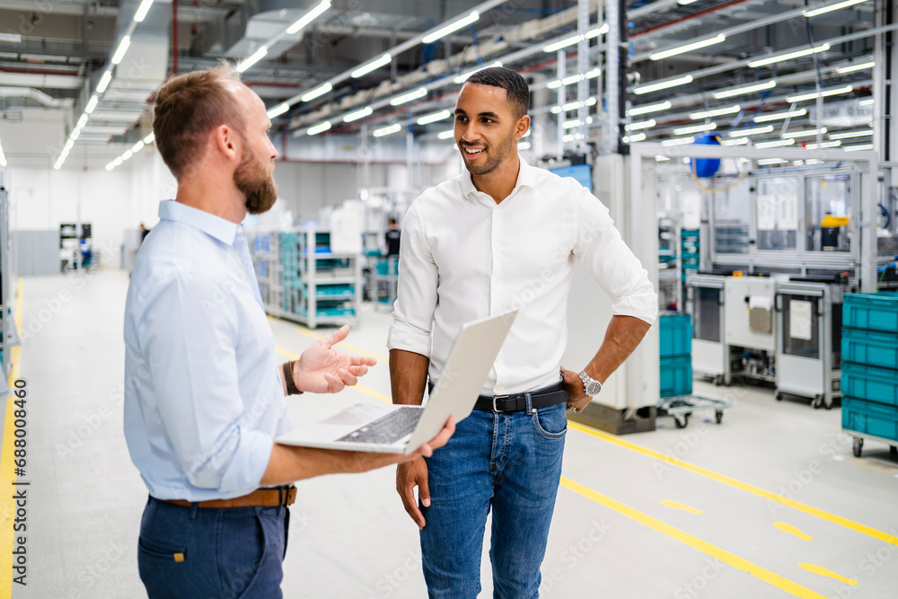 Businessman with laptop and colleague talking in a factory Businessman with laptop and colleague talking in a factory