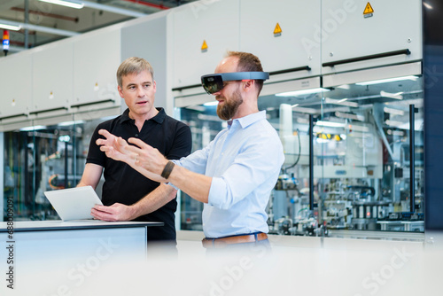 Technician wearing augmented reality glasses in a factory interacting with colleague photo