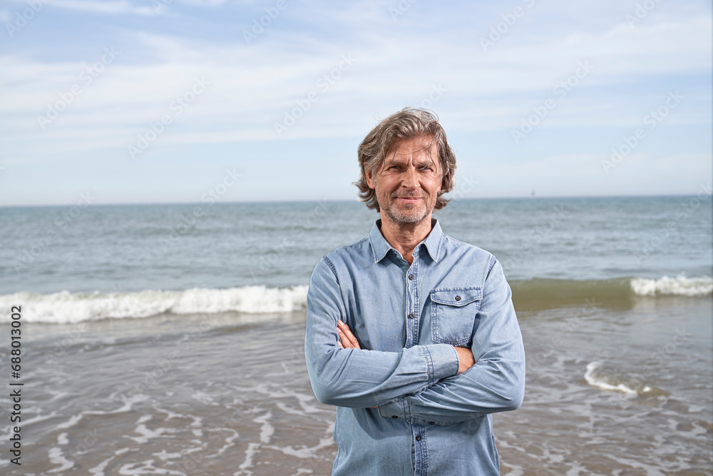 Smiling man standing with arms crossed in front of sea at beach Smiling man standing with arms crossed in front of sea at beach