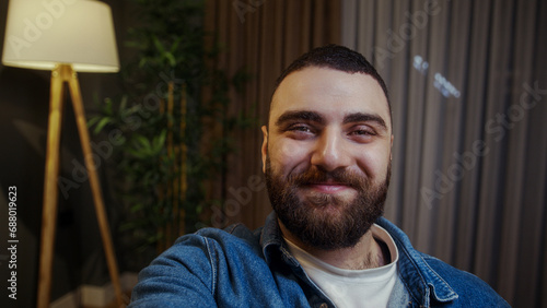 Selfie of confident young adult man holding a smartphone in hand looking at camera making video or selfie