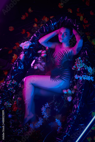 purple and blue light, attractive and young woman lying in bathtub with blooming flowers