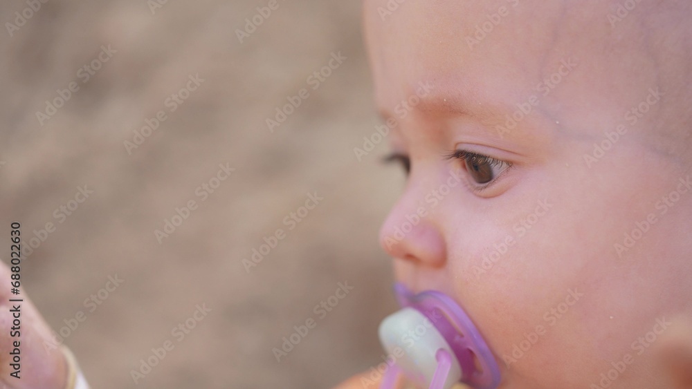 baby baby close-up with a pacifier in his mouth. happy family kid dream concept. baby boy portrait outdoors eyes close-up. baby face sitting on the sand looking lifestyle away baby baby close-up with a pacifier in his mouth. happy family kid dream concept. baby boy portrait outdoors eyes close-up. baby face sitting on the sand looking lifestyle away