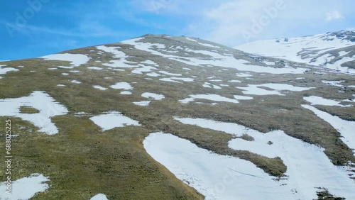Aerial view of high mountains covered with snow with thawing on a sunny day against a blue sky. Deserted gray mountains in winter without grass with snowy peaks. Drone footage. Direct flight. Armenia