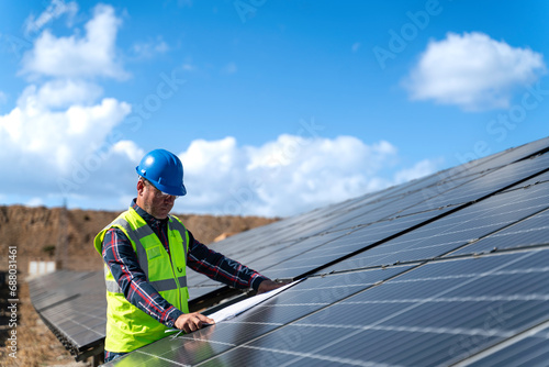 Portrait of male manager engineer in safety helmet checking with blueprint an operation of solar panel system at solar station
