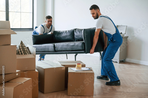 Holding heavy sofa. Two moving service employees in a room photo
