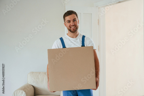 White shirt and blue uniform. With box in hands. Moving service employee in a room © standret