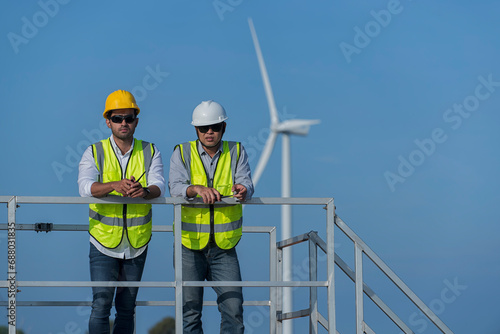 A team of Asian male engineers working together at wind turbine generator farm. Green ecological power energy generation wind sustainable energy concept.