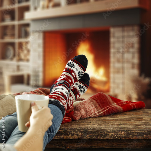 Woman legs with warm winter socks. Home interior with fireplace and empty space for your decoration. Mockup background and december time. Cold winter and new year. 