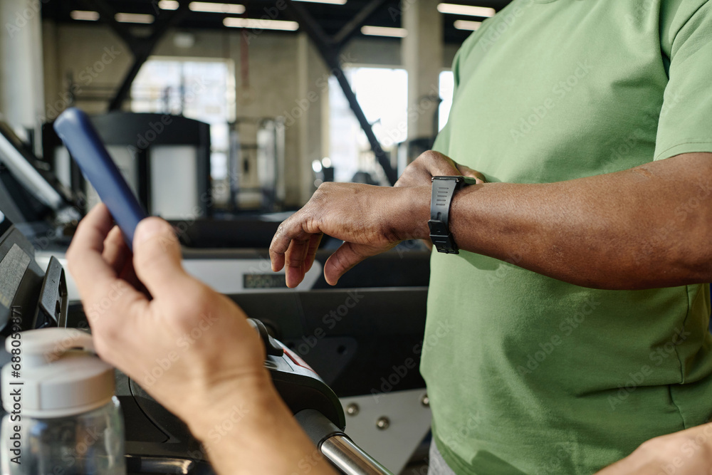 Unknown black man looking at his watch with another caucasian person holding smartphone in hand Unknown black man looking at his watch with another caucasian person holding smartphone in hand