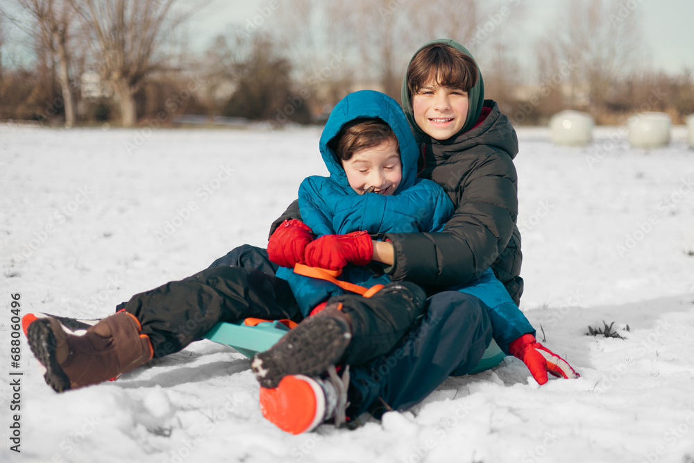 Two happy brothers of different ages are sledding on a clear sunny snowy day.Concept representing winter sports, childhood, leisure activities during the cold season, and family fun. Two happy brothers of different ages are sledding on a clear sunny snowy day.Concept representing winter sports, childhood, leisure activities during the cold season, and family fun.