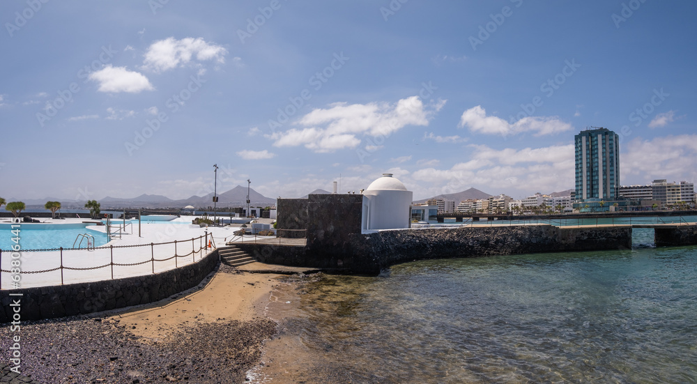 Seascape. View of the city of Arrecife from the islet. White sand beach and jetty. Lanzarote, Canary Islands, Spain.