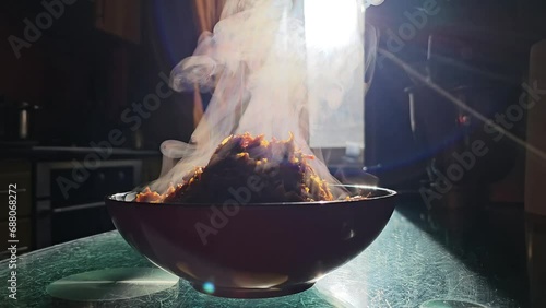 plate with hot steam rises up vegetables porridge carrots fried with onions close-up a lot of steam smoke glass scratched table ordinary kitchen against the background of window sun rays home cooking photo
