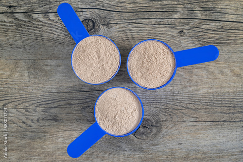 Three supplement scoops in formation filled with protein powder on top of wooden kitchen surface. Dietary supplements concept – flat lay, top view.
