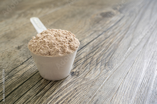 Rounded scoop filled with protein powder on top of clean wooden kitchen surface in natural morning light.