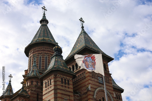 The flag of Timisoara city waving against cloudy sky and Orthodox Cathedral Three Holy Hierarchs. Travel to Romania.